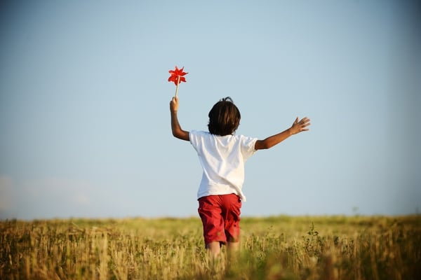 Child walking and running on field holding red spinning flower