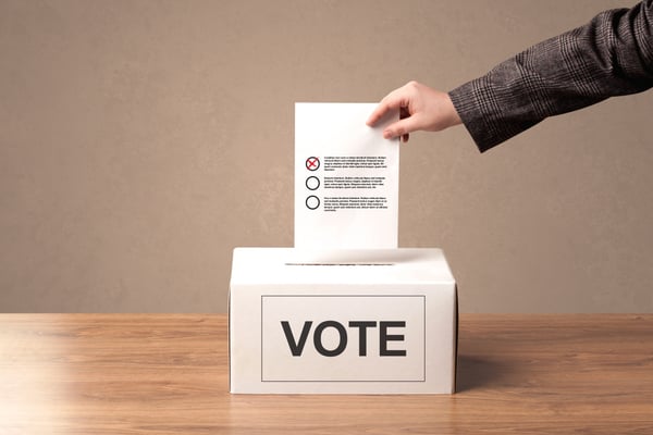 Close up of male hand putting vote into a ballot box, on grungy background