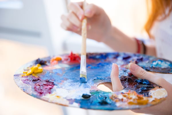 Closeup of paintbrush in woman hands mixing paints on palette