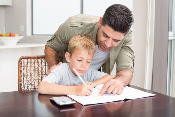 Happy father helping son with math homework at table at home in kitchen