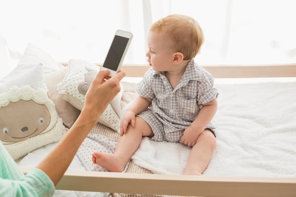 Happy mother using her phone with her baby boy at home in bedroom