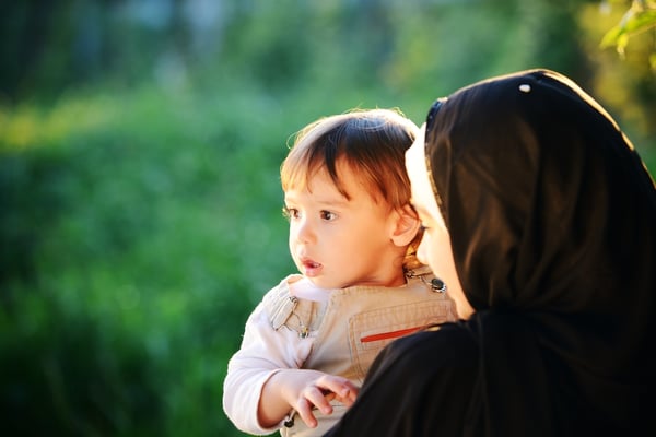 Middle Eastern Muslim mother playing with her little baby in green park and holding him in arms