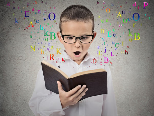 Surprised child reading a book with letters flying away from it isolated on grey wall background. Face expression. Education concept