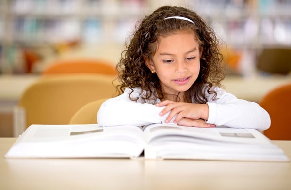 Young school girl reading a book at the library